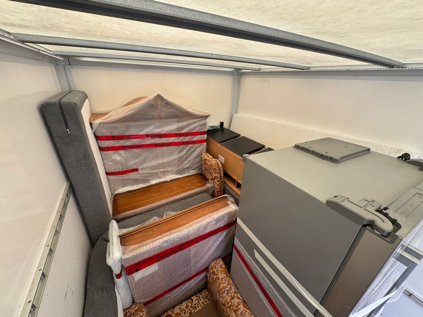 Blick von oben in den Laderaum: in Folie gesicherte Holzmöbel und ein Kühlschrank dicht nebeneinander