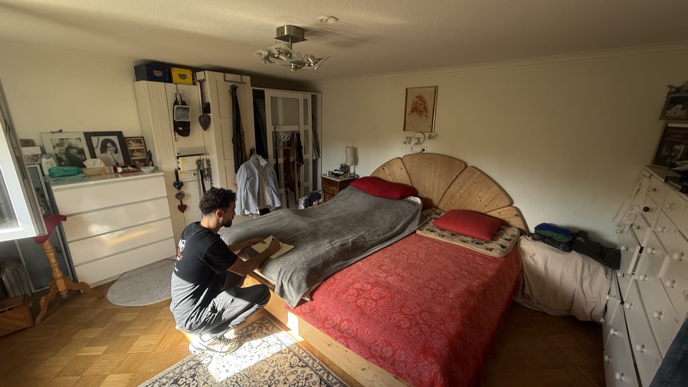 Volles Schlafzimmer in Nehren: Doppelbett mit roter Tagesdecke, weiße Kommode, Kleiderschrank und Bilder an den Wänden