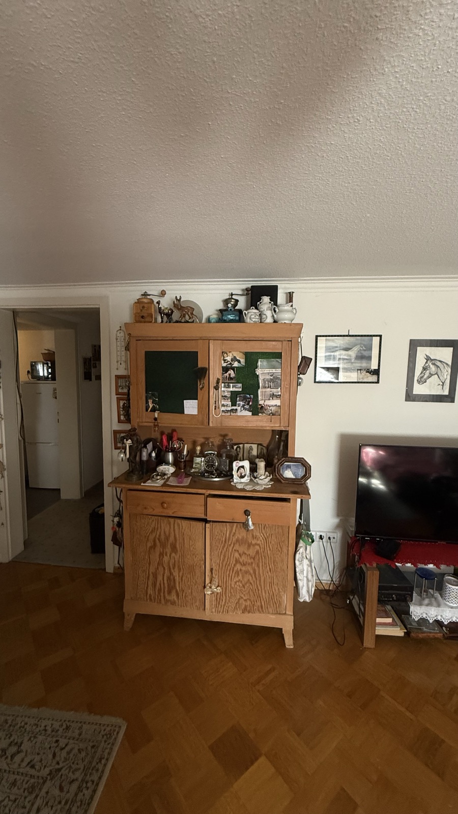 Wohnzimmer mit altem Holzbuffet mit Glasaufsatz, Fernseher und Holzboden